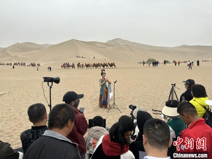 圖為2023年4月底，敦煌大漠“逐舞者”奧楠在鳴沙山月牙泉景區(qū)視頻直播，吸引游人圍觀?！●T志軍 攝